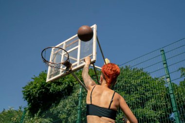 Kısa şortlu, siyah tişörtlü, kısa saçlı, spor sahasındaki aktif eğlence kızı çeviklik antrenmanına basketbol topu atmak için yakın çekim.