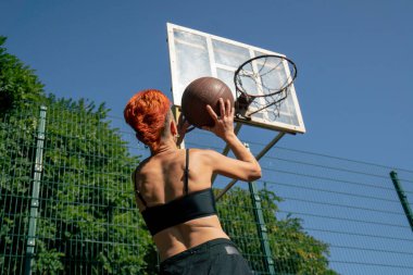 Kısa şortlu, siyah tişörtlü, kısa saçlı, spor sahasındaki aktif eğlence kızı çeviklik antrenmanına basketbol topu atmak için yakın çekim.