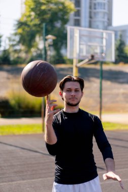 Spor sahasında, beyaz şortlu ve siyah tişörtlü aktif eğlence adamı parmak üstünde basketbol oynuyor.