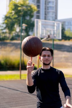 Spor sahasında, beyaz şortlu ve siyah tişörtlü aktif eğlence adamı parmak üstünde basketbol oynuyor.