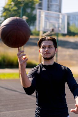 Spor sahasında, beyaz şortlu ve siyah tişörtlü aktif eğlence adamı parmak üstünde basketbol oynuyor.