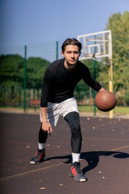 Spor sahası basketbol sahasında beyaz şortlu ve siyah tişörtlü adam kamerada farklı numaralar yapıyor.