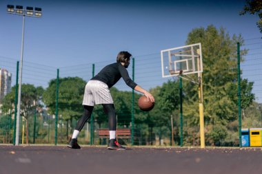 Spor sahası basketbol sahasında beyaz şortlu ve siyah tişörtlü adam kamerada farklı numaralar yapıyor.