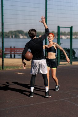 Spor sahası basketbol sahasında kısa şortlu, kısa saçlı, siyah saçlı, basketbol oynayan ve birbirlerine beşlik çakan bir kız.