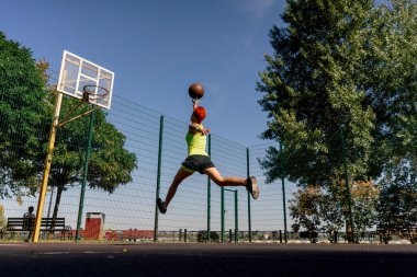Spor sahası basketbol sahasında kısa şortlu ve sarı tişörtlü aktif eğlence kızı yüksek atlama potasına basketbol topu fırlatıyor.