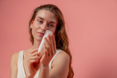 Stüdyo güzelliğini kapat pembe arka plan uzun saçlı kız beyaz krem tüpüyle iç çamaşırıyla poz veriyor doğal güzellik