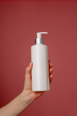 Stüdyonun güzellik çekimini pembe arka planda kadın elleri losyon endüstrisi güzellik salonlarında kullanılacak beyaz bir kap tutuyor.