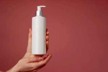 Stüdyonun güzellik çekimini pembe arka planda kadın elleri losyon endüstrisi güzellik salonlarında kullanılacak beyaz bir kap tutuyor.