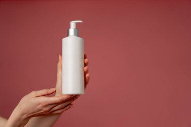 Stüdyonun güzellik çekimini pembe arka planda kadın elleri losyon endüstrisi güzellik salonlarında kullanılacak beyaz bir kap tutuyor.