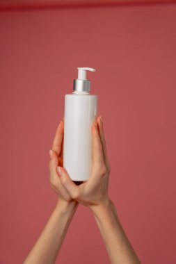 Stüdyonun güzellik çekimini pembe arka planda kadın elleri losyon endüstrisi güzellik salonlarında kullanılacak beyaz bir kap tutuyor.