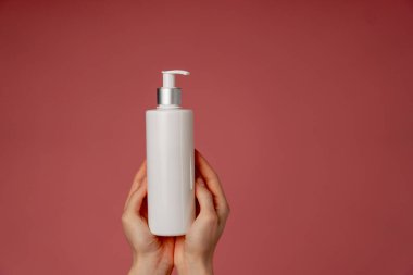 Stüdyonun güzellik çekimini pembe arka planda kadın elleri losyon endüstrisi güzellik salonlarında kullanılacak beyaz bir kap tutuyor.