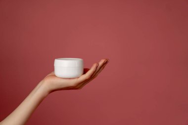 Yakın çekim stüdyo güzellik çekimi pembe arka planda kadın elleri elinde beyaz bir kavanoz yüz kremi güzellik salonu.