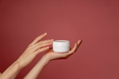 Yakın çekim stüdyo güzellik çekimi pembe arka planda kadın elleri elinde beyaz bir kavanoz yüz kremi güzellik salonu.