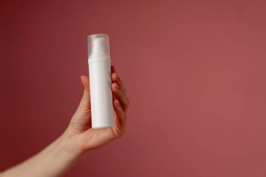 Yakın plan stüdyo güzellik çekimi pembe arka planda kadın elleri uzun beyaz bir kavanoz dolusu yüz kremi güzellik salonu tutuyor.