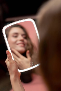 Pembe arka planda bir stüdyonun güzellik çekimi LED ışıklı bir aynaya bakan güzel bir kız cilt değerlendirmesi doğal güzellik kusurlu cilt pozitifliği güzellik salonu