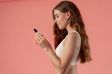 Pembe bir arka planda yakın plan stüdyo güzellik çekimi. Profilde duran güzel bir kız ve gülümseyen kremi inceliyor.