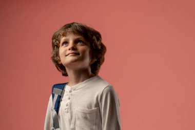 Pembe arka planda bir fotoğraf stüdyosunda on yaşında gülümseyen bir çocuk duruyor. Mavi çantalı bir öğrenci okula hazırlanıyor.