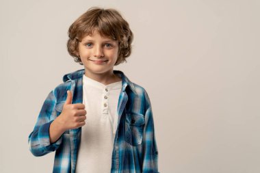 Beyaz arka planda bir fotoğraf stüdyosunda beyaz kazaklı ve mavi kareli gömlekli gülümseyen bir okul çocuğu kameraya bakar.