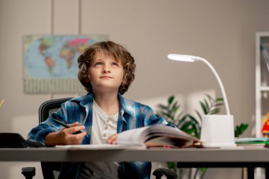 Çocuk odasında beyaz kazaklı ve mavi kareli tişörtlü bir okul çocuğu ders çalışmalarını not defterine yazıp şöyle düşünüyor: