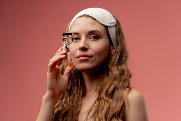 закрыть студию красоты съемки на розовом фоне красивая девушка в белом нижнем белье и маска для сна на голове стоя с ресницами бигуди салон красоты