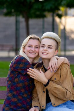 Yazın genç ve güzel sarışın lezbiyen çifti bankta otururken kucaklaşırken ve öpüşürken kameraya bakarken.