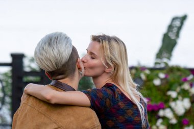 Yazın genç ve güzel sarışın lezbiyen çifti bankta otururken kucaklaşırken ve öpüşürken kameraya bakarken.