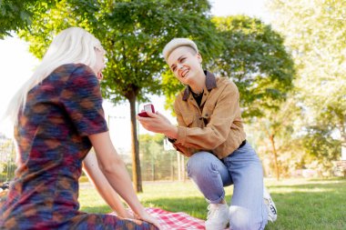 Yazın damalı battaniyede oturan güzel sarışın lezbiyen çift başka bir kıza evlenme teklif ediyor.