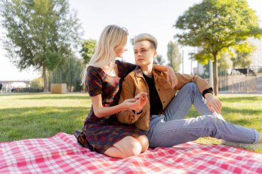 Yazın çimen kareli battaniyenin üzerinde oturan güzel lezbiyen çift birbirine aşık bir çiftin rahatlığı hakkında konuşuyor.