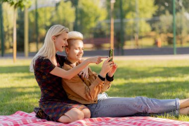 Yazın çimen kareli battaniyenin üzerinde oturmuş birbirine aşık bir çiftin sosyal ağlarda rahatlamasını seyreden güzel bir lezbiyen çift.