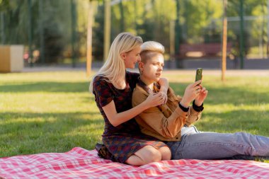 Yazın çimen kareli battaniyenin üzerinde oturmuş birbirine aşık bir çiftin sosyal ağlarda rahatlamasını seyreden güzel bir lezbiyen çift.