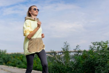 Sokakta nehir kenarında şehir merkezinde beton bir yolda sarı spor takım elbiseli sağlıklı bir kız sabah koşusu yapıyor.