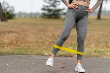 close up on the street in the park in the city center two girls in dark sportswear pumping up their legs and butt with a yellow fitness band