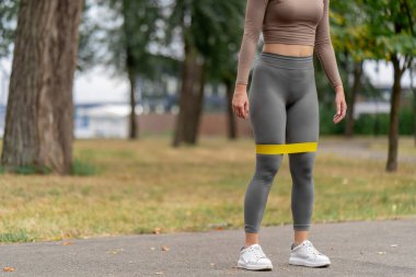 on the street in the park in the city center two girls in dark sportswear pumping up their legs and butt with a yellow fitness band