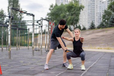 Parkta, yatay barların yanındaki parkta siyah şortlu yakışıklı bir esmer eğitmen ve siyah tişörtlü genç bir kızı eğiten özel spor dersleri tekniği.