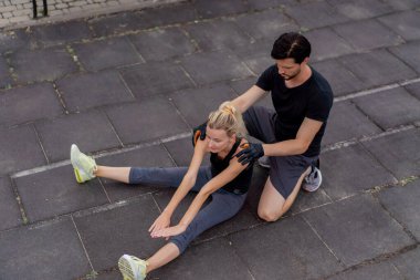 Parkta, yatay barların yanındaki parkta siyah şortlu yakışıklı bir esmer eğitmen ve siyah tişörtlü genç bir kız özel spor dersleri esneklik tekniğini eğitiyor.