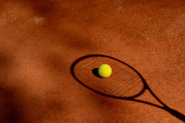 Profesyonel tenis kortunun gölgesinde kırmızı kil yüzey tenis topuyla tenis raketinin üzerinde profesyonel ekipmanlar yatıyor.