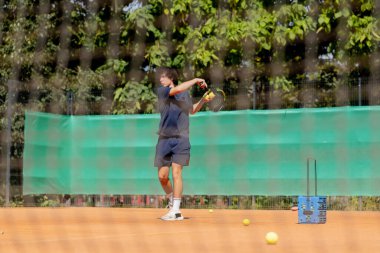 Profesyonel tenis kortunda genç kıvırcık çocuk teknik olarak oyunun ilk servisini yapıyor.