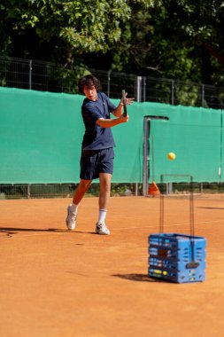 Profesyonel tenis kortunda genç kıvırcık çocuk teknik olarak oyunun ilk servisini yapıyor.