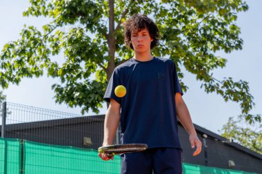 Profesyonel tenis kortunda kendini kaybet. Genç kıvırcık çocuk tenis raketiyle topa vuruyor. Maç için profesyonel hazırlık.