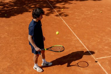 Profesyonel tenis kortunun en iyi atıcısı genç kıvırcık çocuk tenis raketiyle topa vuruyor maç için profesyonel hazırlık.