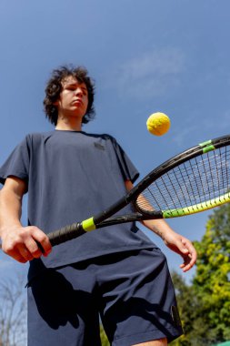 Profesyonel tenis kortuna yakın çekim. Genç kıvırcık çocuk tenis raketiyle topa vuruyor. Maç için profesyonel hazırlık.