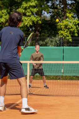 Profesyonel tenis kortunda genç kıvırcık çocuk sarışın rakip çiftle tenis oynuyor aktif dinlenme antrenmanı yapıyor raketle servis yapıyor.