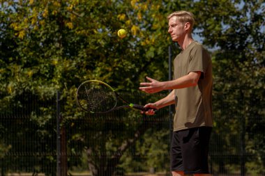 Profesyonel tenis kortunda genç sarışın bir adam tenis topuna vuruyor.