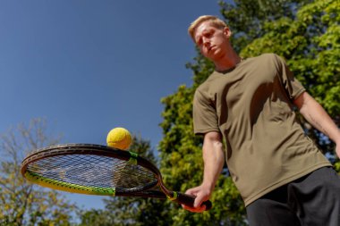 Düşük atımlı profesyonel tenis kortu genç kıvırcık adam tenis raketiyle topa vuruyor maç için profesyonel hazırlık.