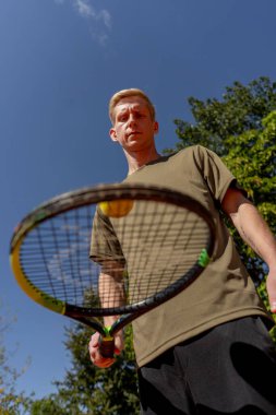 Düşük atımlı profesyonel tenis kortu genç kıvırcık adam tenis raketiyle topa vuruyor maç için profesyonel hazırlık.