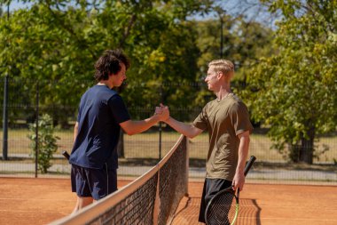 Profesyonel tenis kortunda genç, kıvırcık bir adam sarışın rakip çiftle el sıkışıyor. Aktif eğlence eğitimi alıyor. Kazanan belli.