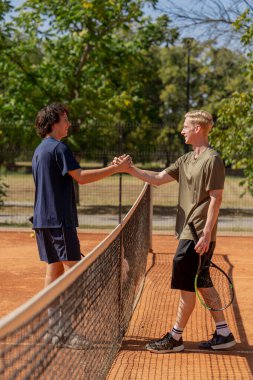 Profesyonel tenis kortunda genç, kıvırcık bir adam sarışın rakip çiftle el sıkışıyor. Aktif eğlence eğitimi alıyor. Kazanan belli.