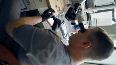 Diş protozoası kaplaması üretimi için dikey video profesyonel laboratuarı ve erkek uzman büyüteçlerle diş şeklini parlatıyor.