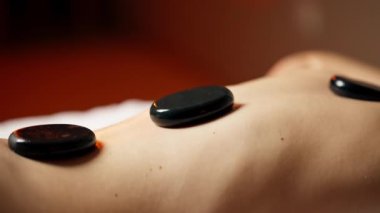 Masaj masasının üstündeki masaj salonunda siyah taşlarla çıplak sırt masajı yapan bir kız özel bölgelerde dinleniyor.