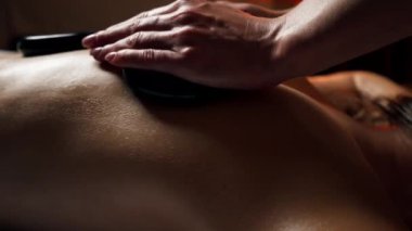 Masaj masasının üstündeki masaj salonunda siyah taşlarla çıplak sırt masajı yapan bir kız özel bölgelerde dinleniyor.